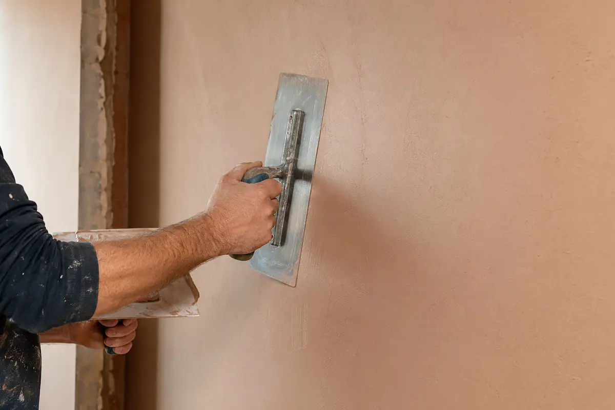 Close view of a steel trowel smoothing fresh finishing plaster on an interior wall